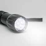 A black flashlight is turned on, emitting a bright white light, akin to essential risk prevention resources. It’s positioned on a smooth, light gray surface, with the focus on the front where the beam shines brightly.